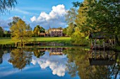 PRIORS MARSTON, WARWICKSHIRE: VIEW ACROSS LAKE, POND, WATER TO HOUSE, SPRING, MAY, BOATHOUSE, BOAT, HOUSE, REFLECTIONS REFLECTED, CLOUDS