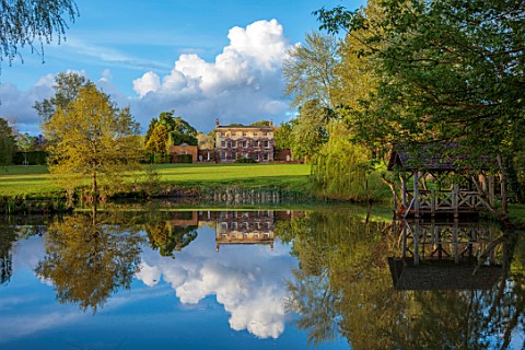 PRIORS_MARSTON_WARWICKSHIRE_VIEW_ACROSS_LAKE_POND_WATER_TO_HOUSE_SPRING_MAY_BOATHOUSE_BOAT_HOUSE_REF