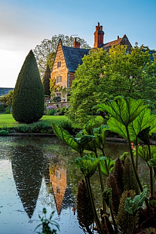 COTON_MANOR_NORTHAMPTONSHIRE_THE_MANOR_HOUSE_SEEN_FROM_THE_POOL_POND_WATER_LAKE_SPRING_MAT_GUNNERA_M