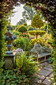 THE LASKETT GARDENS, HEREFORDSHIRE. DESIGNER ROY STRONG - VIEW THROUGH HEDGE, BENCH, BENCHES, PATHS, CLIPPED TOPIARY, SUMMER, JULY, SUNRISE, DAWN, SERPENTINE WALK