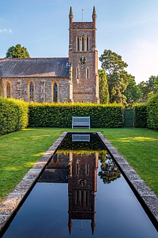 STOCKCROSS_HOUSE_BERKSHIRE_LONG_NARROW_BLACK_POOL_WITH_CHURCH_REFLECTED_IN_IT_WOODEN_BENCH_LAWN_HEDG