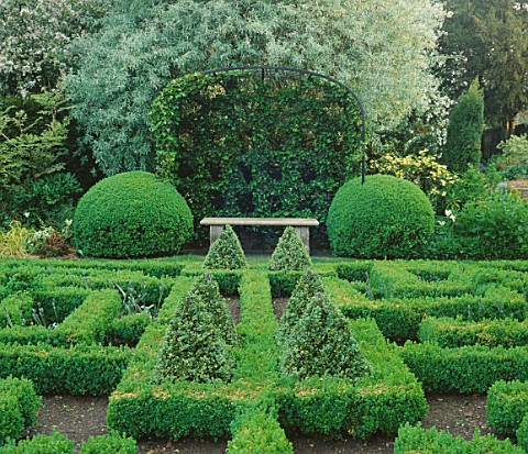 STONE_BENCH__HEDERA_PARSLEY_CRESTED_ON_METAL_FRAME_BEHIND_BOX_BALLS_AT_SIDE_IN_THE_KNOT_GARDEN_AT_BO