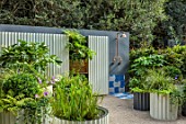 CHELSEA 2021 - THE HOT TIN ROOF GARDEN, DESIGNER ELLIE EDKINS: WHITE STEEL CONTAINERS PLANTED WITH FATSIA, FERNS, GERANIUMS, BOX, BUXUS, COURTYARD, TERRACE, WALLS, OUTDOOR SHOWER