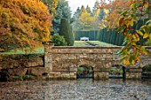 THENFORD GARDENS & ARBORETUM, NORTHAMPTONSHIRE: AUTUMN, OCTOBER, BRIDGE, RILL, ACER PALMATUM, ACERS, MAPLES, POOL, POND, LAKE, WATER, CLIPPED TOPIARY, BENCH, SEAT