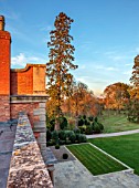 MORTON HALL, WORCESTERSHIRE: FALL, AUTUMN, EVENING LIGHT, SUNSET, VIEW EAST TOWARDS PARKLAND, LAWN, CLIPPED TOPIARY, SCOTS PINE, PINUS SYLVESTRIS