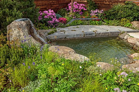 CHELSEA_2022_A_SWISS_SANCTUARY_BY_LILLY_GOMM_METAL_SEAT_BENCH_RHODODENDRONS_GRAVEL_PATHS_ROCKS_WATER