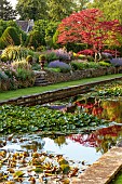 THE SUMMERHOUSE, OXFORDSHIRE: JULY, SUMMER, VIEW ALONG CANAL, POND, POOL, WATER, GARDEN, BORDERS, MAPLES, TREES, WATERLILIES, STEPS, URNS, CONTAINERS, WALLS, REFLECTIONS