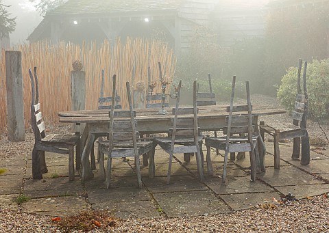 LONGYARD_COTTAGE_ESSEX_WINTER_FEBRUARY_MIST_FOG_FOGGY_LAWN_WOODEN_TABLE_CHAIRS_CUT_MISCANTHUS_STEMS_