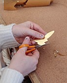 JESS WHEELER, NORTH WALES: JESS WHEELER IN HOME STUDIO, USING A PAIR OF EMBROIDERY SCISSORS TO CUT OUT LEAF SHAPES