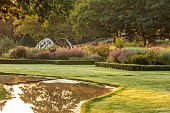 GRANTLEY HALL, YORKSHIRE: DAWN, BOX EDGED BEDS, WATER, POOL, LAWN, PATINATED STEEL AND COLOURED STAINLESS STEEL GLAZED CUPOLA SEAT, RILL, BORDERS, GRASSES, SEPTEMBER