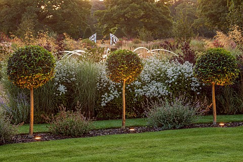 GRANTLEY_HALL_YORKSHIRE_LOLLIPOP_TOPIARY_IN_LAWN_BORDER_WITH_ASTERS_FOUNTAIN_BEHIND