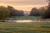COTTESBROOKE HALL AND GARDENS, NORTHAMPTONSHIRE: VIEW FROM SOUTH TERRACE OVER LAKE TO BRIXWORTH CHURCH, SUNRISE, MARCH, SPRING, BORROWED LANDSCAPE