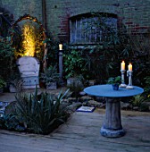 NIGHT-LIT CORNER OF GARDEN WITH CERAMIC CHAIR & GLASS/CERAMIC TABLE WITH CANDLES. DESIGNER: EMMA LUSH. WATER FEATURE BY MARK LAURENCE