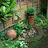 WATER FEATURE: WALL MOUNTED CERAMIC TOAD WATER SPOUT ABOVE BRICK EDGED PEBBLE POND. DESIGNER: LUCY SMITH