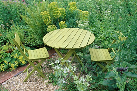A_PLACE_TO_SIT_GREEN_TABLE__CHAIRS_STAND_ON_GRAVEL_AMONGST_EUPHORBIA_WULFENII__ALCHEMILLA_MOLLIS__ER