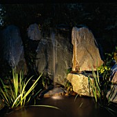 NIGHT-LIT WATER FEATURE: SIMPLE FOUNTAIN OVER ROCKS INTO POOL. LIGHTING BY GARDEN & SECURITY LIGHTING. NATURAL & ORIENTAL WATER GARDENS  HAMPTON COURT 97.