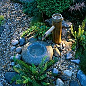 JAPANESE WATER FEATURE: BAMBOO WATER SPOUT INTO STONE BOWL.  LIGHTING BY GARDEN & SECURITY LIGHTING. NATURAL & ORIENTAL WATER GARDENS  HAMPTON COURT 97.