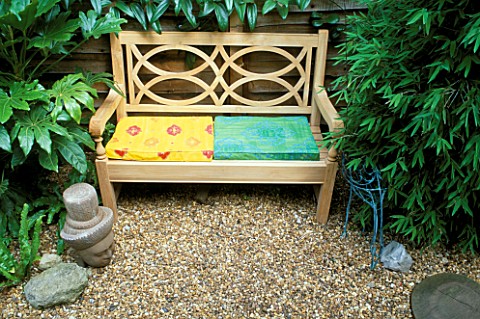 TROPICAL_GARDEN_WITH_WOODEN_BENCH_AND_BRIGHTLY_COLOURED_CUSHIONS__WITH_BUDDHAS_HEAD__WIRE_BIRD__FATS