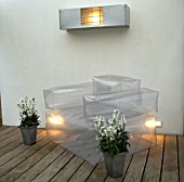 METAL CONTAINERS WITH WHITE NIGHT SCENTED STOCKS STAND BESIDE INFLATABLE   CHAIR ON WOODEN DECKING IN CHARLES WORTHINGTONS MINIMALIST GARDEN. (NIGHT-LIT) DESIGNER:STEPHEN WOODHAMS
