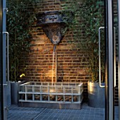 WATER FEATURE: WATER SPOUT CASCADES ONTO SEA-WORN PEBBLES IN FOUNTAIN BASE OF  TRANSPARENT GLASS BRICKS. DESIGNER STEPHEN WOODHAMS OWN GARDEN.