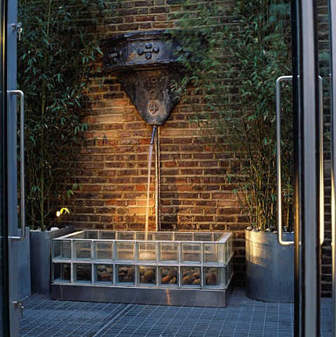 WATER_FEATURE_WATER_SPOUT_CASCADES_ONTO_SEAWORN_PEBBLES_IN_FOUNTAIN_BASE_OF__TRANSPARENT_GLASS_BRICK
