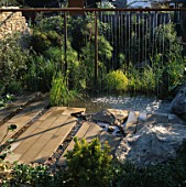 WATER CURTAIN FEATURE FLOWING FROM A RUSTY SCAFFOLDING POLE INTO POOL WITH ROCKS AND PAVING. ISRAEL JUBILEE GARDEN. DES: DAVID STEVENS. CHELSEA 1998