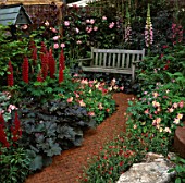 BRICK PATH LEADS THROUGH RED THEMED COTTAGE BORDERS OF LUPINS & AQUILEGIAS TO SECLUDED WOODEN BENCH. DESIGNER: JOHN PLUMMER. CHELSEA 1993