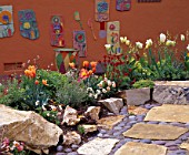 PUMPKIN COLOURED WALL WITH CERAMIC PICTURES. IN FOREGROUND ARE ORANGE TULIPS AND ARIZONA FLAG STONE AND MEXICAN COBBLES. KEEYLA MEADOWS  CALIFORNIA