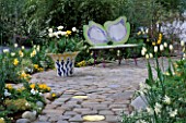 DOGWOOD BUTTERFLY BENCH BY KEEYLA MEADOWS BESIDE A CERAMIC POT PLANTED WITH WHITE TULIPS. DESIGNER: KEEYLA MEADOWS CALIFORNIA