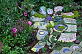 BRIGHTLY PAINTED CERAMIC HEADS AND STEPPING STONES SURROUNDED BY RANUNCULUS. DESIGN BY KEEYLA MEADOWS SAN FRANCISCO