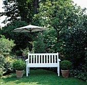 A PLACE TO SIT: SECLUDED WHITE BENCH SEAT ON LAWN WITH BOX BALLS IN POTS EITHER SIDE. SHADY GARDEN PARASOL IN B/G