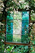 TURQUOISE STAINED GLASS PANEL BY JOANNA HARDING SURROUNDED BY JASMINUM OFFICINALE. DESIGNER: ALEX JEFFERSON.