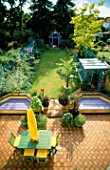 VIEW OVER THE NICHOLS GARDEN WITH TERRACOTTA PATIO  GREEN TABLE AND CHAIRS  ORANGE SUN SHADE  TRACHYCARPUS FORTUNEI  GREENHOUSE  GAZEBO AND LILAC DECKED SANDPIT & POOL