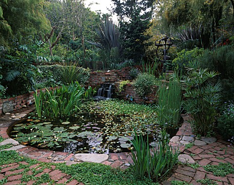 LARGE_CIRCULAR_POOL_SURROUNDED_BY_LUSH_PLANTING_INCLUDING_PHORMIUMS_AND_BRONZE_FERTILITY_GODDESS_FOU