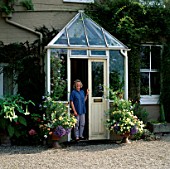 JENNY JOWETT STANDING IN HER PORCH SURROUNDED BY CONTAINERS OF VERBENS PEACHES AND CREAM  PLUMBAGO AND ARGYRANTHEMUM JAMAICA PRIMROSE