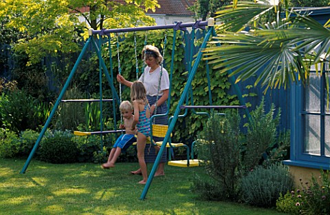 HAZEL__ROBERT_AND_JANE_PLAYING_ON_THE_SWING_WITH_BLUE_FENCE_AND_GOLDEN_HOP___NICHOLS_GARDEN__READING