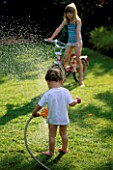 HAZEL AND WILLIAM PLAYING WITH A HOSEPIPE IN THE GARDEN. THE NICHOLS GARDEN  READING