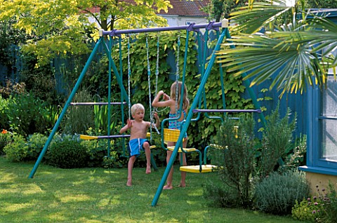 HAZEL_AND_ROBERT_PLAYING_ON_THE_SWING_WITH_THE_BLUE_FENCE_AND_GOLDEN_HOP_BEHIND_THE_NICHOLS_GARDEN__