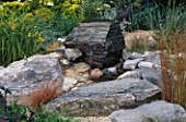 WATER FEATURE: NATURAL LOOKING ROCK POND WITH BOULDER FOUNTAIN SURROUNDED BY GRASSES IN SACRED GARDENS/CLEVER DECKS FENG SHUI GARDEN. HAMPTON 1999.