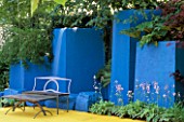 A PLACE TO SIT: CONTEMPORARY METAL GARDEN FURNITURE AGAINST VIVID BLUE WALLS AND YELLOW CONCRETE FLOOR WITH HOSTAS. CITROEN UKS CITROEN IN BLOOM. HAMPTON 1999