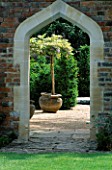 ARCHWAY IN BRICK WALL LOOKING THROUGH TO TERRACOTTA CONTAINERS HOLDING WISTERIA STANDARDS. THE ABBEY HOUSE  WILTSHIRE.