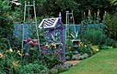 COVERED SEAT PAINTED MAUVE SURROUNDED BY METAL URNS PAINTED SILVER WITH AGAVES  SILVER METAL OBELISKS  ALLIUM CHRISTOPHII  HEMEROCALLIS  CARDOON AND ERIGERON. THE NICHOLS GARDEN