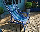 A PLACE TO SIT: BLUE STRIPED CANVAS DECKCHAIR ON RIBBED DECKING. IN B/G IS PAINTED SHED AND METAL CONTAINERS OF TOPIARY. ROBIN GREEN & RALPH CADES SEASIDE STYLE GARDEN  LONDON.