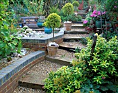 WOODEN SLEEPERS EDGE STEPS THROUGH THE GARDEN WITH STANDARD CLIPPED TREES AND OLD GARDEN TOOLS LINING THE PATH. ROBIN GREEN AND RALPH CADES SEASIDE STYLE GARDEN  LONDON.
