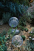 ALUMINIUM GLOBES STANDING ON GRAVEL AND SURROUNDED BY GREY GRASSES  CONVULULUS CNEORUM AND LOBELIA SIPHILITICA . ROBIN GREEN AND RALPH CADES SEASIDE STYLE GARDEN  LONDON
