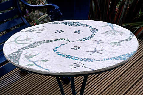DETAIL_OF_BLUE_AND_WHITE_MOSAIC_TABLE_STANDING_ON_RIBBED_DECKING_ROBIN_GREEN_AND_RALPH_CADES_SEASIDE