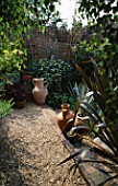 VIEW ACROSS SHINGLE & STEPS LINED WITH SLEEPERS TO THE WICKER AND BAMBOO FENCE. WITH TERRACOTTA URNS & PHORMIUM ATROPURPUREUM. ROBIN GREEN & RALPH CADES SEASIDE STYLE GDN  LONDON.