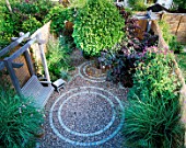 SMALL GARDEN WITH CIRCULAR BRICK PATTENS IN GRAVEL. WITH NATURAL WOODEN SWING SEAT AND STOOL  VERBENA BONARIENSIS AND CLEMATIS. BAMBOO FENCING CREATES AN ATTRACTIVE BORDER.