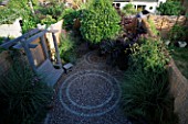 OVERVIEW OF SMALL GARDEN WITH CIRCULAR BRICK PATTENS IN GRAVEL. NATURAL WOODEN SWING SEAT AND STOOL  VERBENA BONARIENSIS & CLEMATIS. BAMBOO FENCING CREATES AN ATTRACTIVE BORDER.