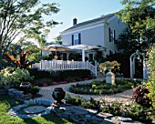 VIEW ACROSS GARDEN TOWARDS WHITE HOUSE WITH VERANDAH  CANVAS PARASOL AND URNS ON DRY STONE WALL.  BILL SMITH AND DENNIS SCHRADERS GARDEN  LONG ISLAND  USA